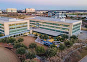 Thumbnail 23 of 24 - A large, modern building with a parking lot in front.