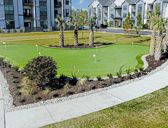 A golf green is surrounded by sand bunkers and palm trees at Evolve St. James Apartment Homes Apartments, Southport, NC, 28461
