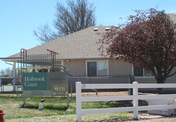 A sign for Holbrook Court apartments is in front of a building.