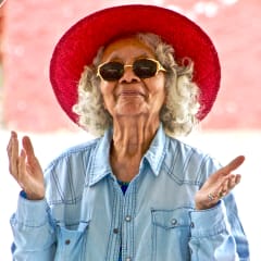 an older woman wearing a red hat and blue shirt with her hands in the air