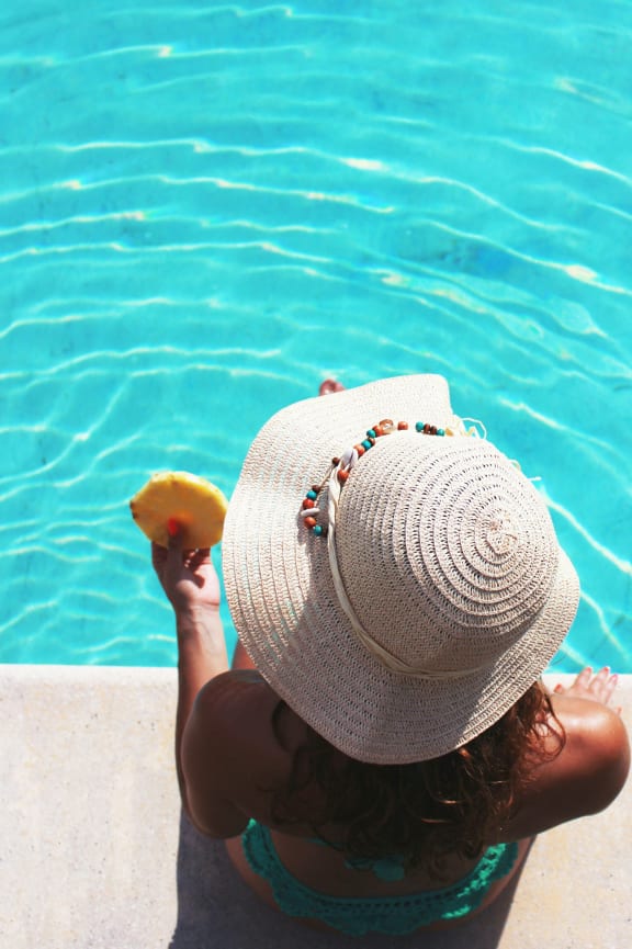 a woman in a hat holding a piece of fruit by a pool