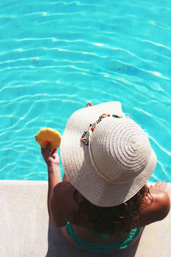 A woman in a straw hat is sitting by a pool.