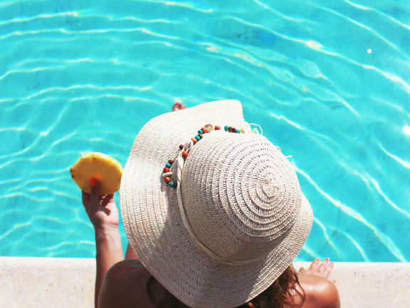 a woman in a hat holding a piece of fruit by a pool