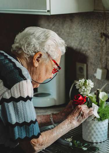 An elderly woman arranging flowers in a pot.