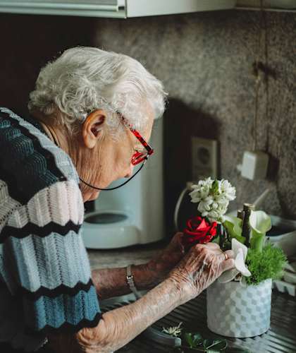 An elderly woman arranging flowers in a pot.