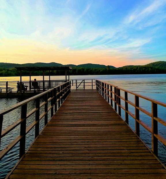 A wooden pier extends into a calm body of water under a sky with scattered clouds.