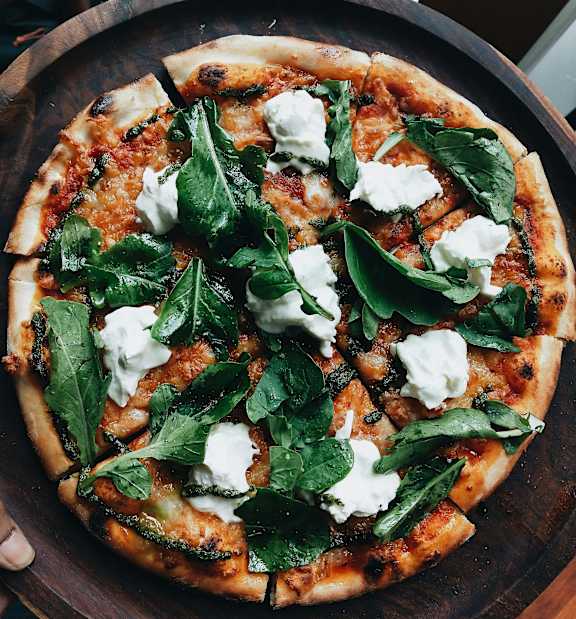 A pizza with spinach and white topping on a wooden board.