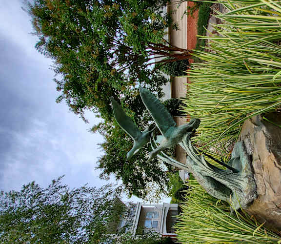 A green statue of a bird is in the middle of a garden.