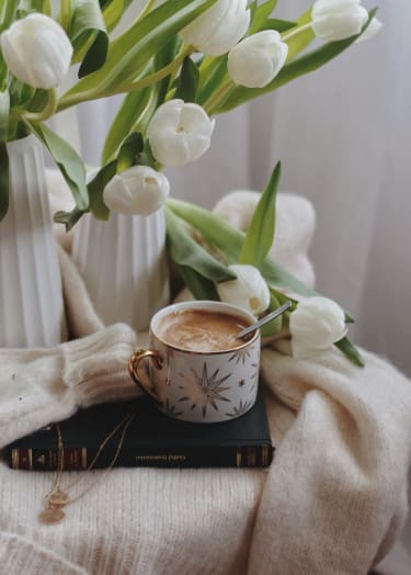 a cup of coffee next to white tulips and a book at 505 Collection in Georgia 30305