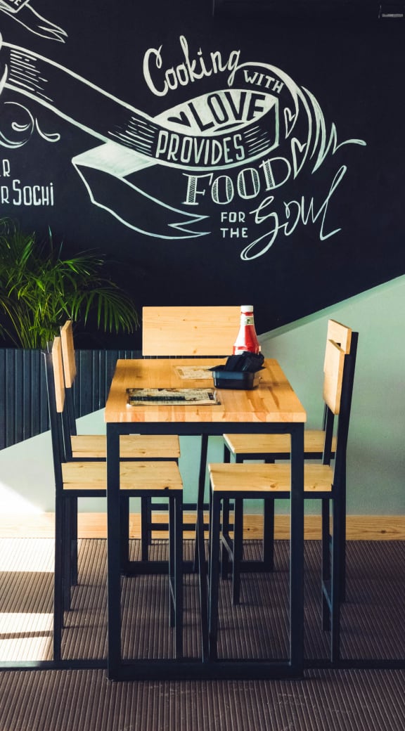 a wooden table with chairs in front of a wall with a painting on it