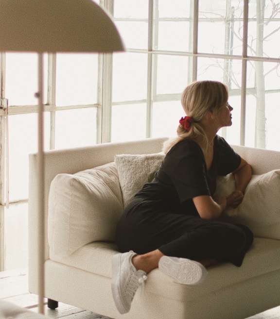 A woman in a black outfit is sitting on a white couch.