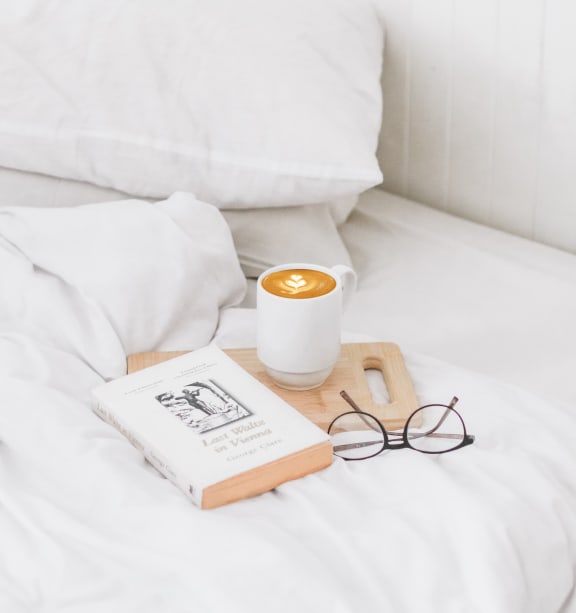 a cup of coffee and a book on a tray on a bed