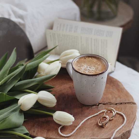 a cup of coffee and white tulips on a wooden board