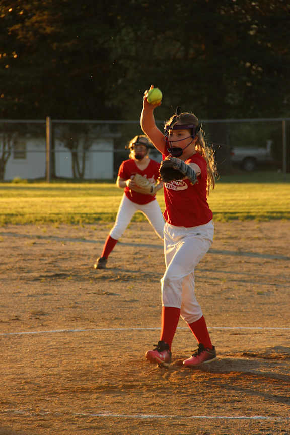 A girl in a red shirt throws a ball while another girl in a white shirt and red socks catches it.