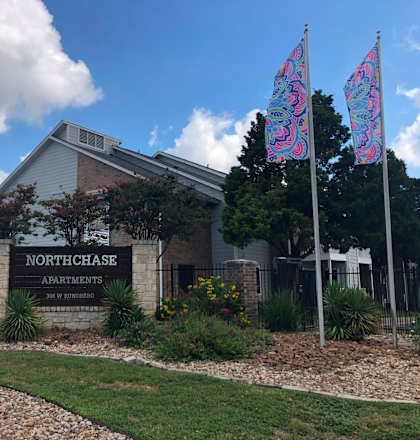 The image shows the front of Northchase Apartments with a sign and two decorative flags.