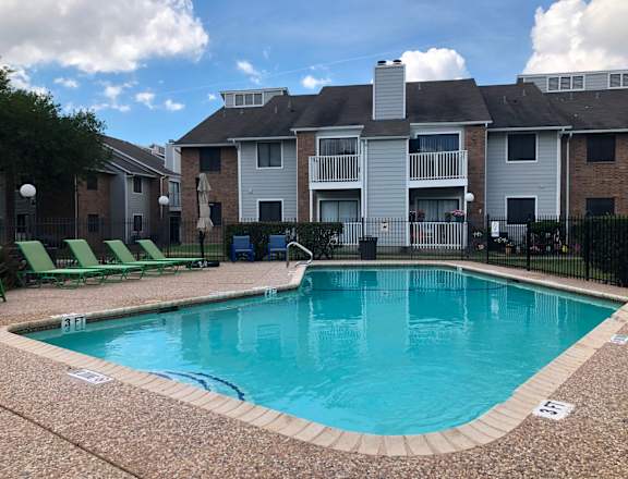A swimming pool surrounded by a black fence and green lawn chairs.