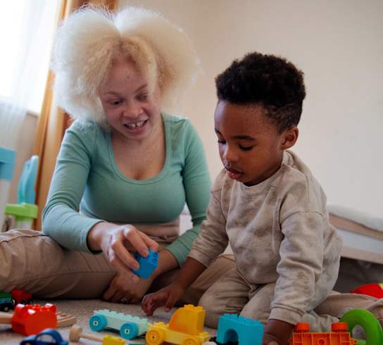 A woman and a child are playing with toy cars on the floor.