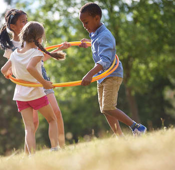 Children playing with a hula hoop in a grassy field.