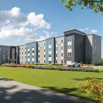 A modern building with a grey and blue exterior is surrounded by greenery and a clear blue sky. at Heritage Landing Apartments, Terre Haute, 47803
