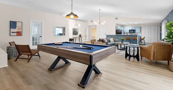 A pool table is in the middle of a room with a chair and a plant.