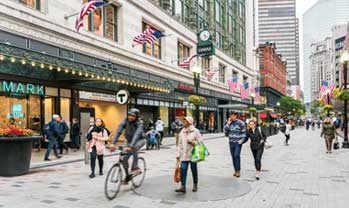 A busy street scene with people walking and a cyclist.