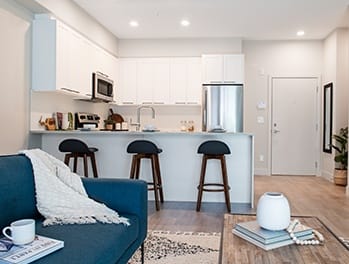 a small living room with a couch and three stools in front of a kitchen with a