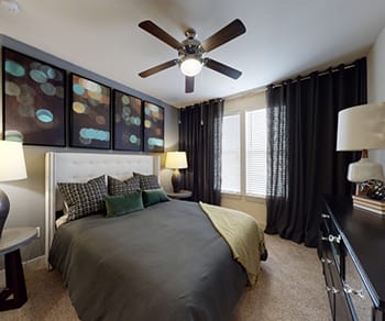 A bedroom with a king-size bed with dark bedding, a window, dresser, and nightstands at Four Seasons. 