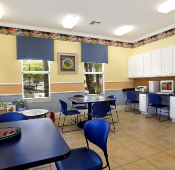 a room with a table and chairs and a kitchen in the background