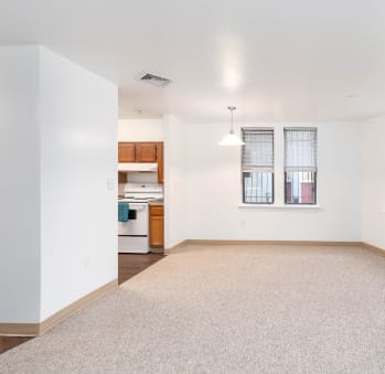 an empty living room with a kitchen in the background