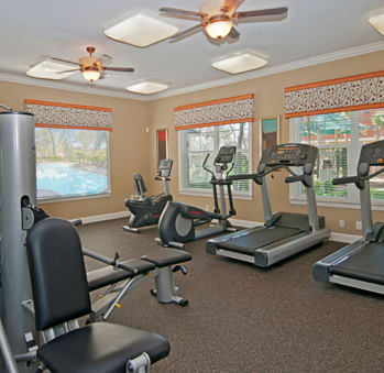 a room filled with cardio equipment and windows with a pool in the background