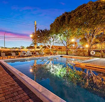 A pool surrounded by trees and lights at dusk.