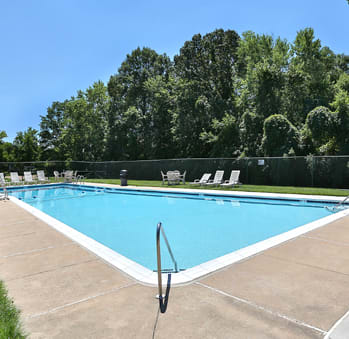 a swimming pool with chaise lounge chairs and trees in the background