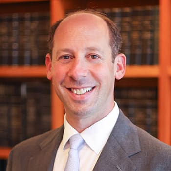 a man in a suit and tie smiles in front of a bookshelf