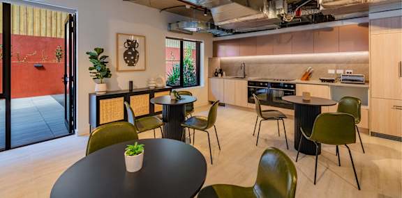 a dining room with tables and chairs and a kitchen in the background