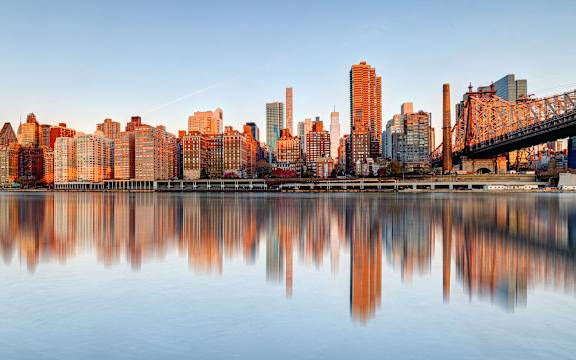 A city skyline is reflected in the water in front of it.