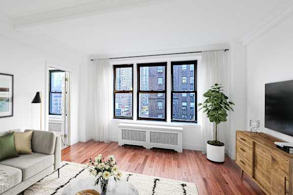 A living room with a grey couch, a white bench, a television, and a plant.at Sutton Collection, New York, NY