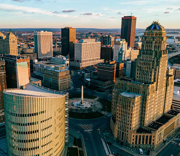 A cityscape with a mix of modern and older buildings, a river in the background, and a clear sky.