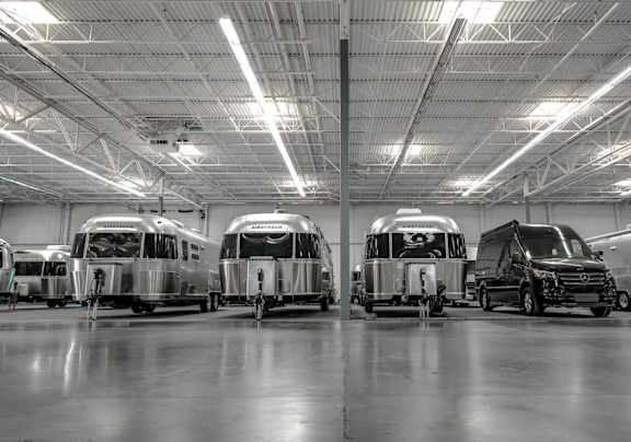 Several airstreams and a large sprinter vehicle parked in an indoor storage space. 