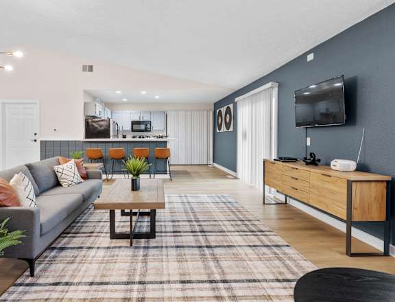 A living room with a grey couch, a coffee table, and a flat screen TV mounted on the wall.