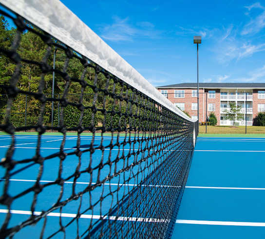 A tennis court with a black net and a building in the background.