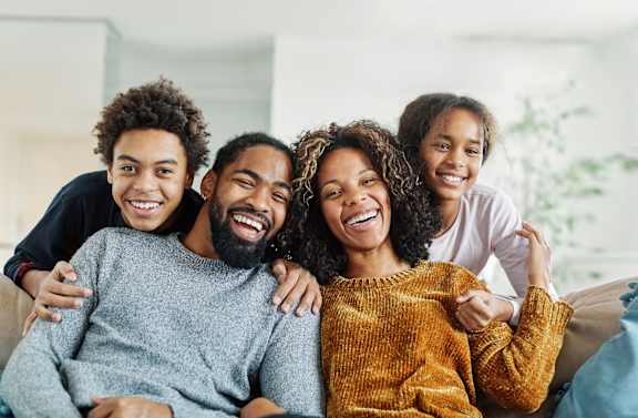 A family of four is sitting closely together on a couch.