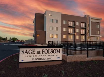 a sign in front of a building with a sunset in the background