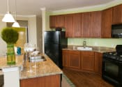 Thumbnail 5 of 23 - kitchen at VistaView apartments in Frederick, MD with black appliances, dark wood cabinets and flooring, kitchen island with sink and counter seating and stone countertops at VistaView, Frederick