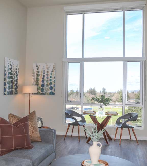 A living room with a grey couch and a large window.