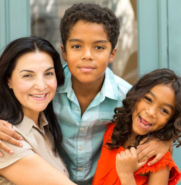 A woman and two children are standing in front of a window.
