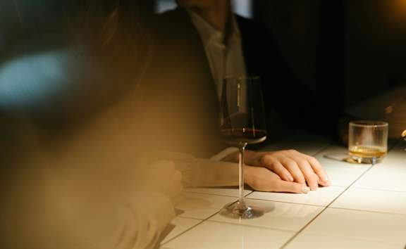 A man and a woman are sitting at a table with a glass of wine in front of them.