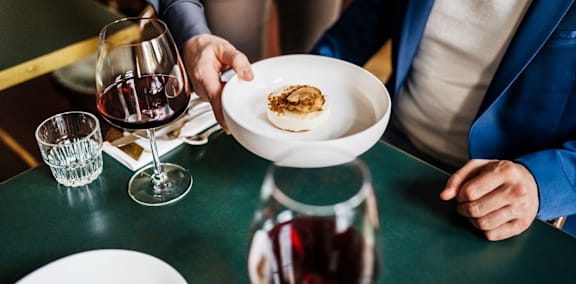 A person is holding a plate with food and a glass of wine on the table.