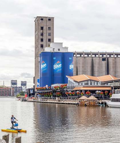 A large blue building with the word "blue" on it is in the background of a body of water with a boat and people on paddleboards.