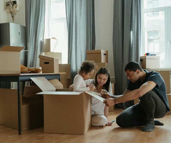 a man and woman sitting on the floor with boxes and a child looking at a