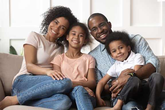 A family of four is sitting closely together on a couch.